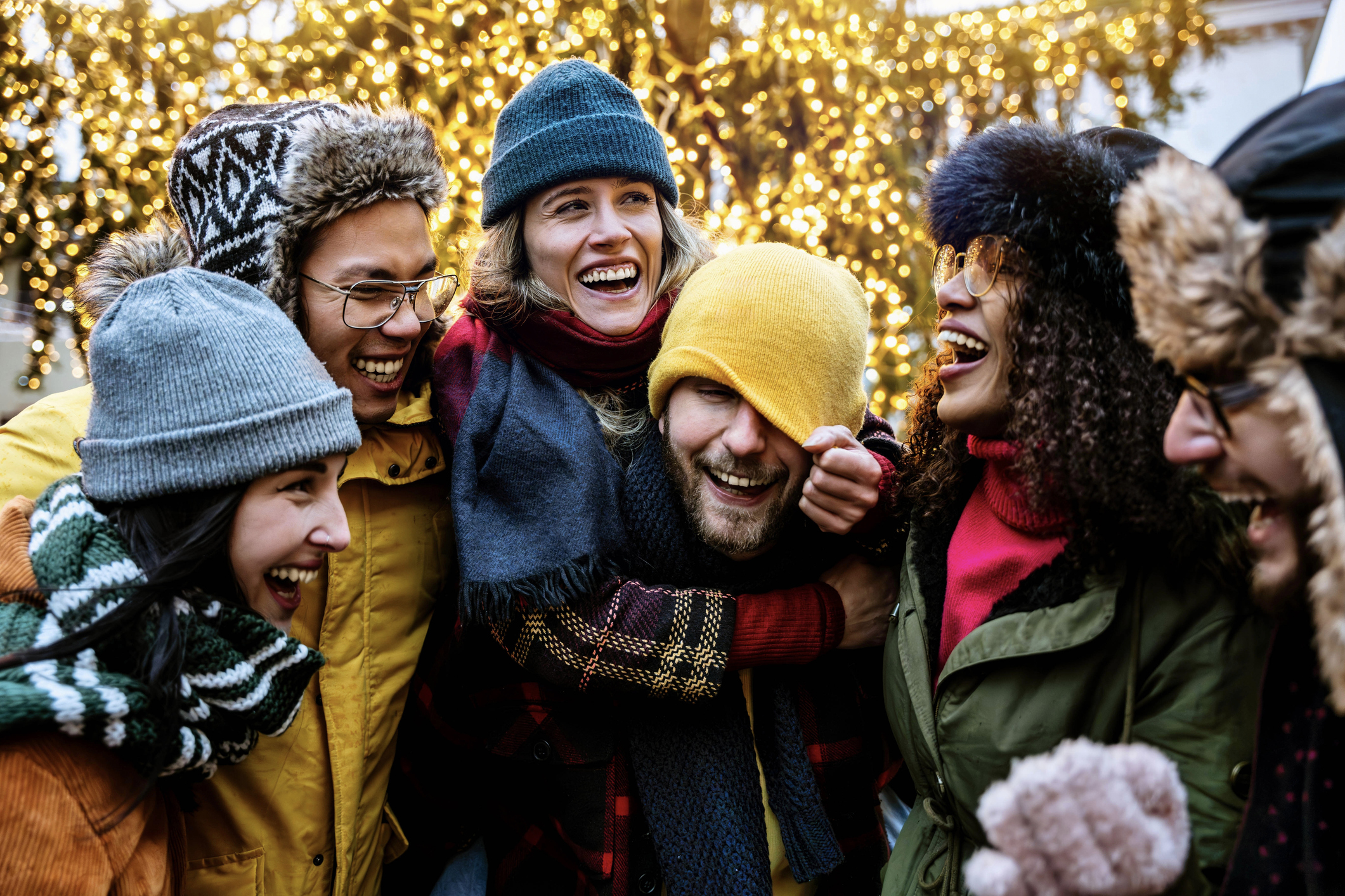 A group of friends in beanies and scarfs laughing together outside.