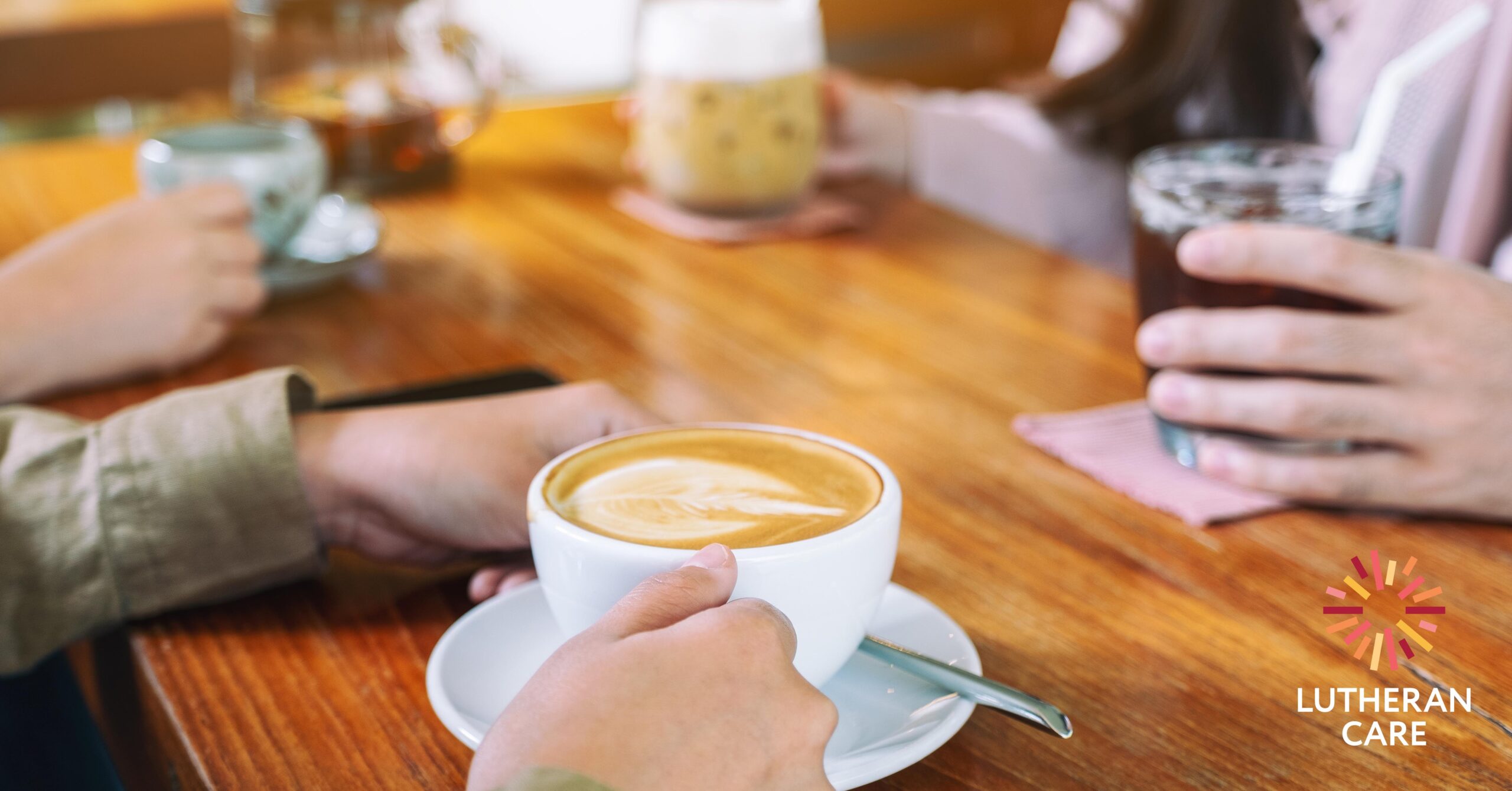 Close up of a coffee table where a group of people are drinking coffees together. The Lutheran Care logo appears on the right hand side of the image.