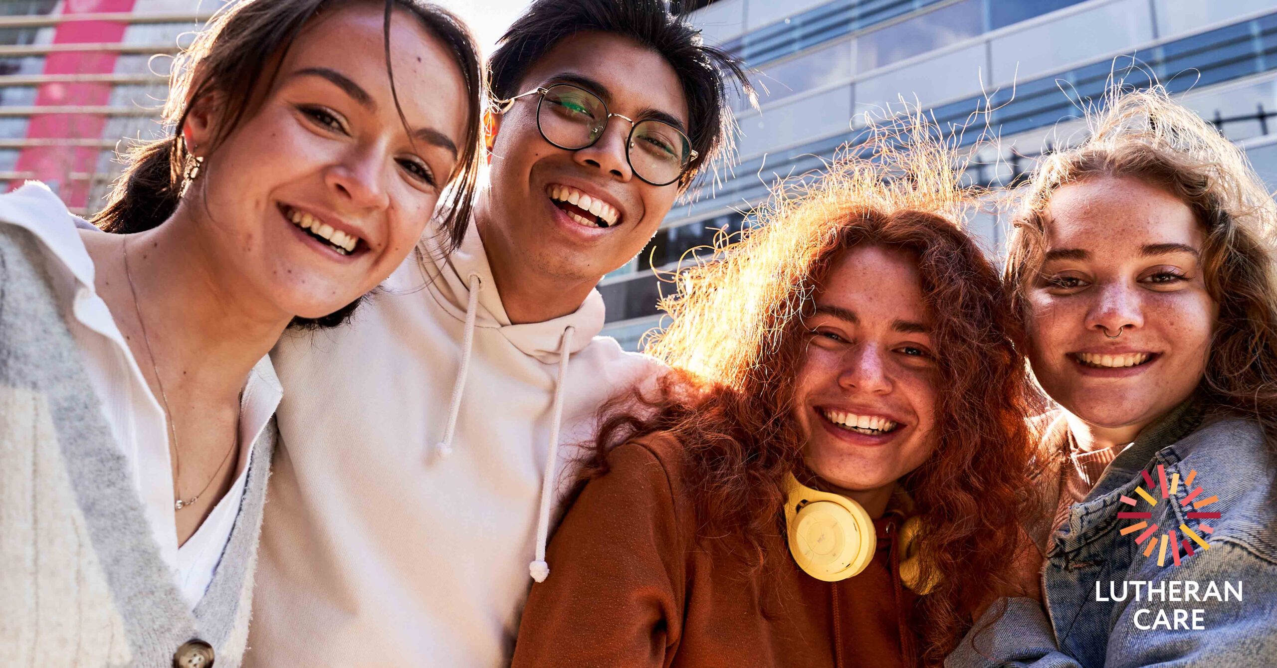 A group of teenagers hugging and smiling at the camera. The Lutheran Care logo appears in the bottom right hand corner.