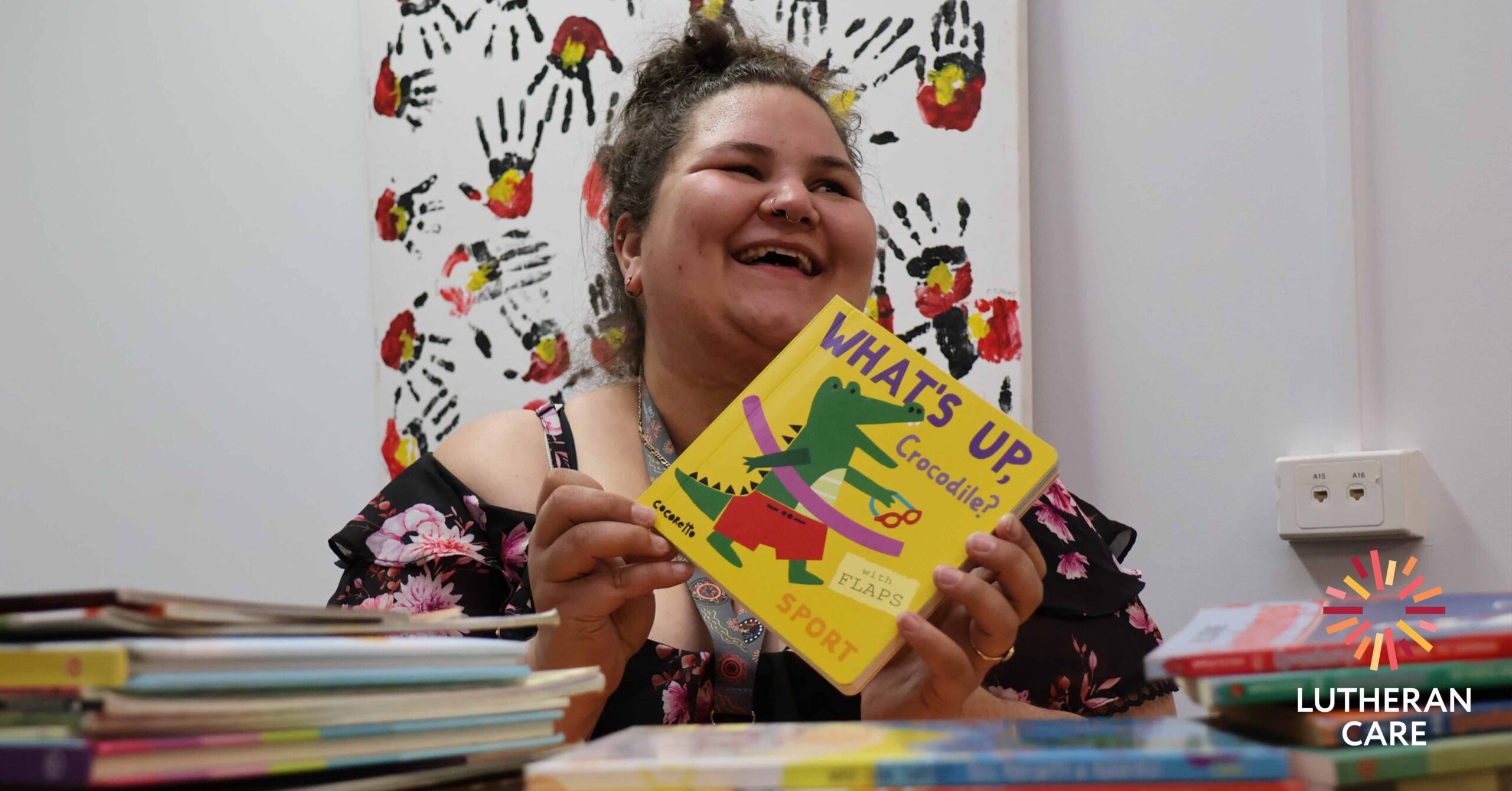 Lutheran Care staff member Emily with book donated. The Lutheran Care logo appears in the bottom right hand corner.