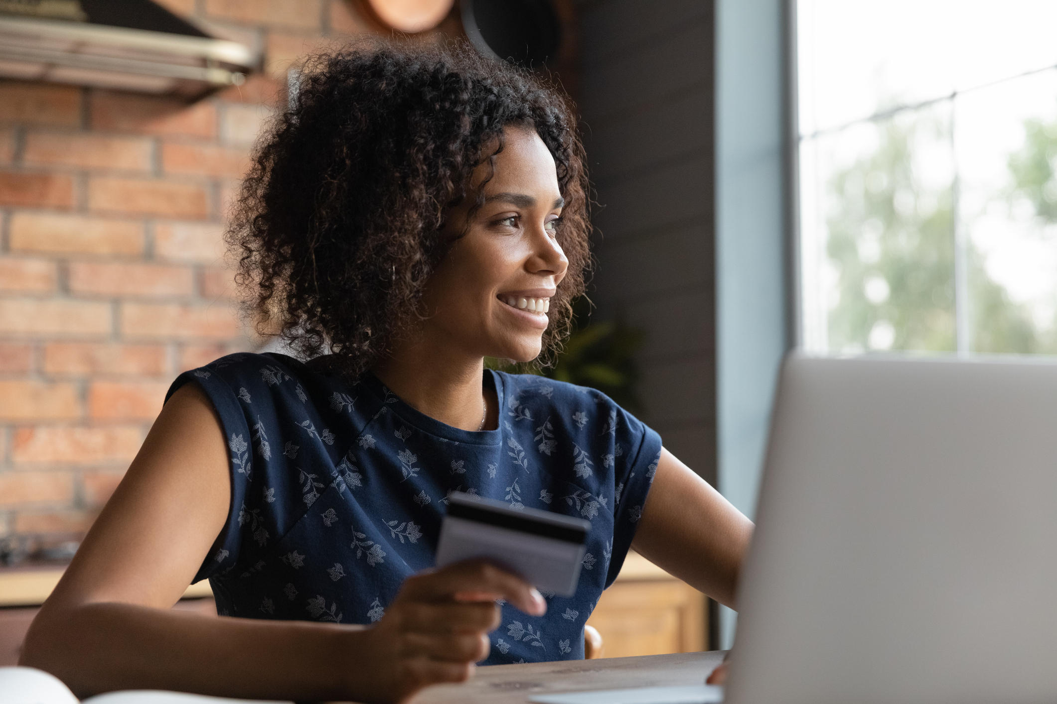 Young woman is sitting at her computer with a bank card in hand paying bills.