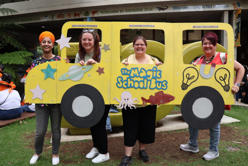 Staff dressed up for the All Staff Day 2024 with a cut out school bus from a children's adventure show.