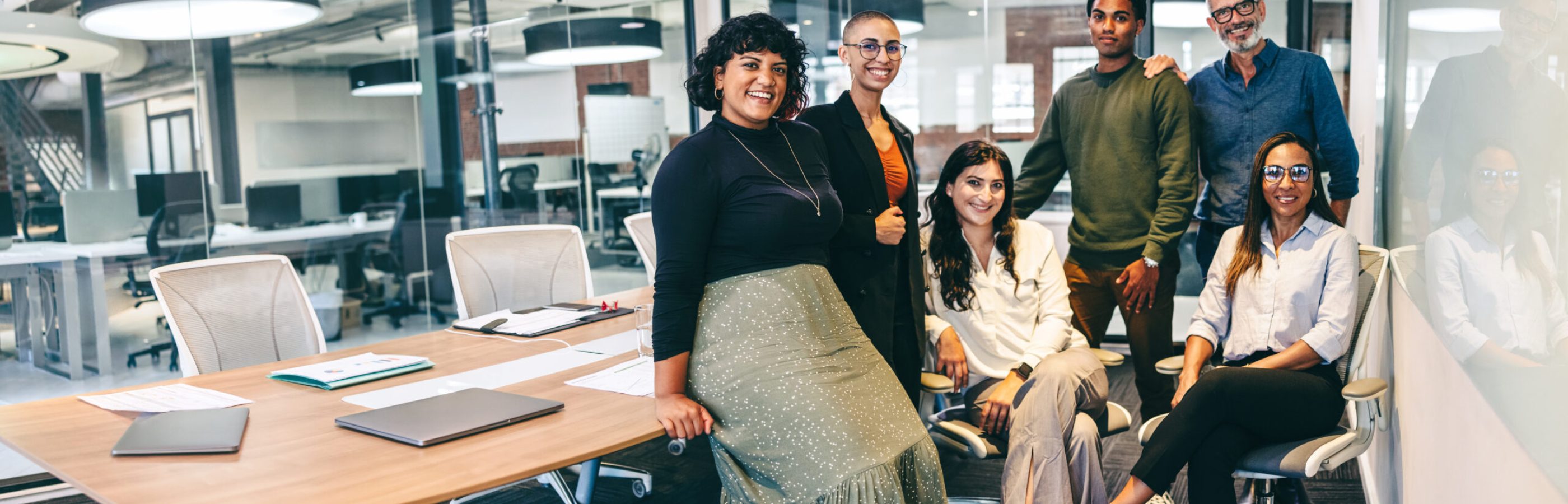 Team of businesspeople smiling at the camera in a boardroom. Cheerful businesspeople grouped together in a modern workplace. Diverse team of businesspeople looking cheerful.