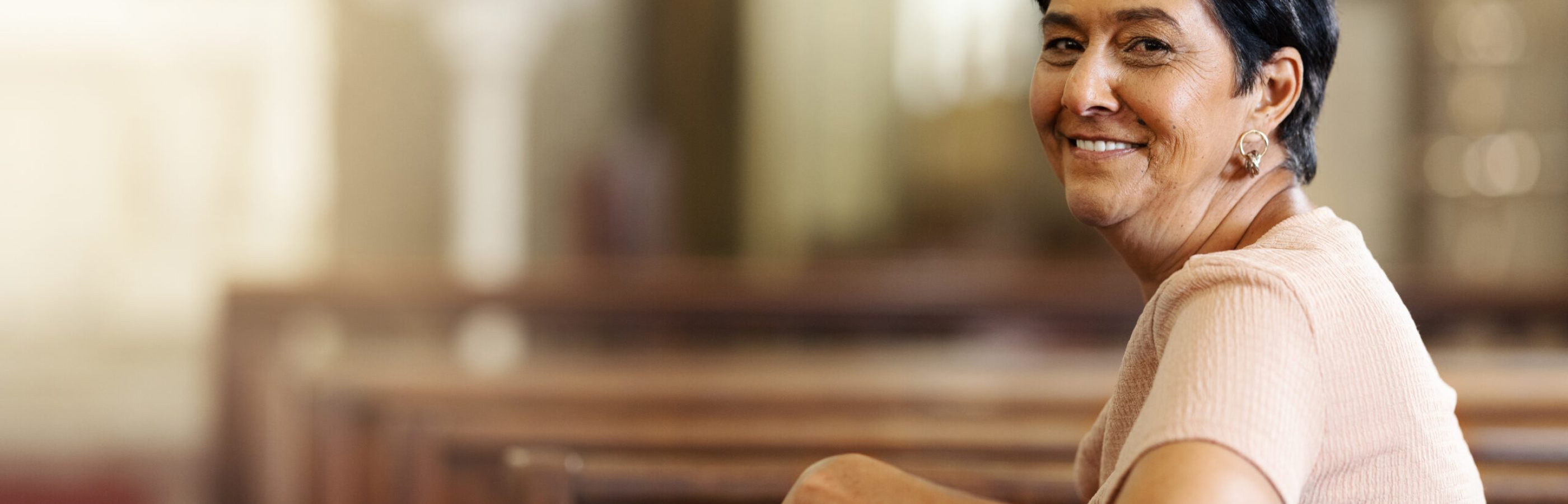 Woman sitting in church pew smiles at camera.